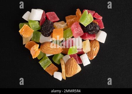 Diät-Food-Konzept zum Valentinstag. Getrocknete Früchte und Nüsse in Form eines Herzens, isoliert auf schwarzem Hintergrund, Draufsicht, Nahaufnahme, Makro Stockfoto