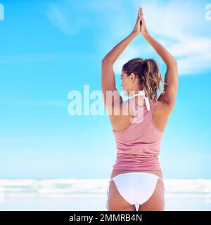 Mit Yoga lebt man besser. Eine junge Frau, die am Strand Yoga macht. Stockfoto