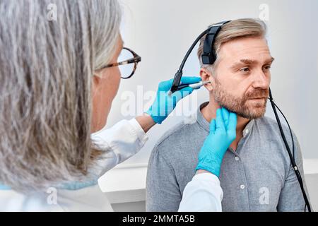 Gutaussehender Mann während Tympanometrie oder Impedanzaudiometrie und Prüfung der Mittelohrfunktion mit dem Tympanometer-Schallkopf in der Hörklinik Stockfoto