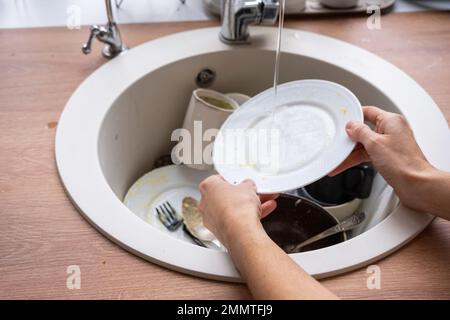 Frauenhände waschen den Teller unter fließendem Wasser. Dreckiges Geschirr im Waschbecken in der Küche, Chaos nach dem Mittagessen, zu faul, um Geschirr abzuspülen. Küchenreinigung Stockfoto