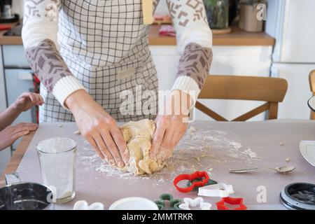 Hände kneten dicken Teig auf den Küchentisch, dekoriert mit festlichen Dekorationen zu Weihnachten und Neujahr. Backen zu Hause, Aroma und Komfort. Schließen- Stockfoto