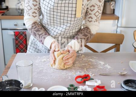 Hände kneten dicken Teig auf den Küchentisch, dekoriert mit festlichen Dekorationen zu Weihnachten und Neujahr. Backen zu Hause, Aroma und Komfort. Schließen- Stockfoto