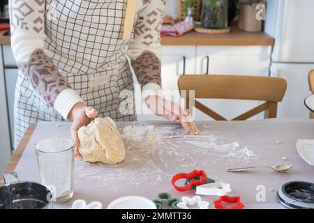 Hände kneten dicken Teig auf den Küchentisch, dekoriert mit festlichen Dekorationen zu Weihnachten und Neujahr. Backen zu Hause, Aroma und Komfort. Schließen- Stockfoto