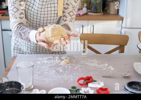 Hände kneten dicken Teig auf den Küchentisch, dekoriert mit festlichen Dekorationen zu Weihnachten und Neujahr. Backen zu Hause, Aroma und Komfort. Schließen- Stockfoto