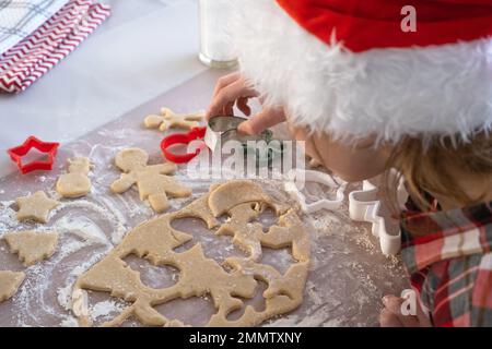 Die Hände von mutter und Tochter schneiden Kekse aus dem Teig heraus, mit Schimmelpilzen auf einem Weihnachtsmotiv in Form eines Schneemanns, eines Weihnachtsbaums, Sterns Stockfoto
