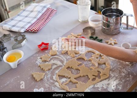 Die Hände von mutter und Tochter schneiden Kekse aus dem Teig heraus, mit Schimmelpilzen auf einem Weihnachtsmotiv in Form eines Schneemanns, eines Weihnachtsbaums, Sterns Stockfoto