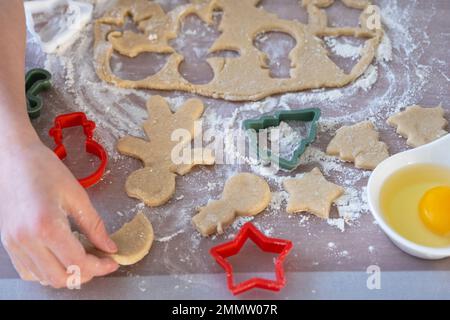 Die Hände von mutter und Tochter schneiden Kekse aus dem Teig heraus, mit Schimmelpilzen auf einem Weihnachtsmotiv in Form eines Schneemanns, eines Weihnachtsbaums, Sterns Stockfoto