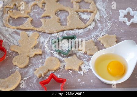Die Hände von mutter und Tochter schneiden Kekse aus dem Teig heraus, mit Schimmelpilzen auf einem Weihnachtsmotiv in Form eines Schneemanns, eines Weihnachtsbaums, Sterns Stockfoto