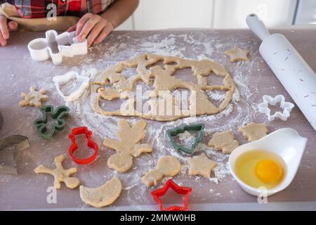 Die Hände von mutter und Tochter schneiden Kekse aus dem Teig heraus, mit Schimmelpilzen auf einem Weihnachtsmotiv in Form eines Schneemanns, eines Weihnachtsbaums, Sterns Stockfoto
