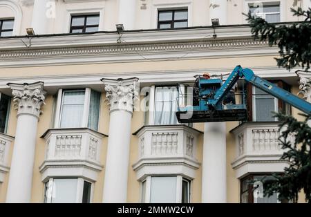 Arbeiter in der Kranhalle, Restaurierung der alten Fassade des historischen Gebäudes. Bauarbeiter in der Höhe, die an einem Kran in der Hubschaufel arbeiten. Stockfoto