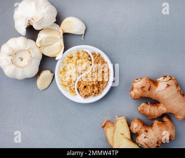 Knoblauch und Ingwer, ganz und zerdrückt, liegen flach auf Grau Stockfoto