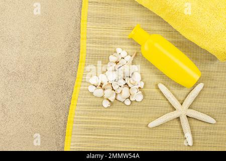 Weißes Herz aus Muscheln mit Seestern und einer gelben Flasche Sonnencreme und Handtuch auf Strohliegen auf Sand. Konzepturlaub, Valentinstag, holi Stockfoto