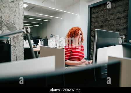 Junge Geschäftsfrau, die an einem Desktop-Computer in einem modernen Startup-Büro arbeitet Stockfoto