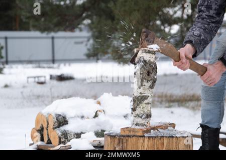 Ein Mann hackt Feuerholz mit einer Axt im Winter draußen im Schnee. Alternative Heizung, Holzernte, Energiekrise Stockfoto