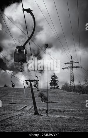 Skilift im Stillstand aufgrund von Schneemangel infolge des Klimawandels am Ende des Winters auf einem Hügel in Münsingen, Schwäbische Alb, Deutschland. Stockfoto