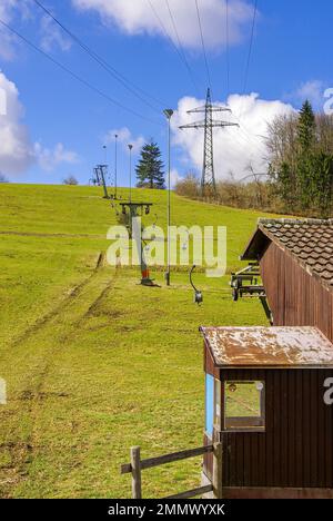 Skilift im Stillstand aufgrund von Schneemangel infolge des Klimawandels am Ende des Winters auf einem Hügel in Münsingen, Schwäbische Alb, Deutschland. Stockfoto