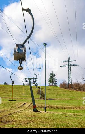 Skilift im Stillstand aufgrund von Schneemangel infolge des Klimawandels am Ende des Winters auf einem Hügel in Münsingen, Schwäbische Alb, Deutschland. Stockfoto