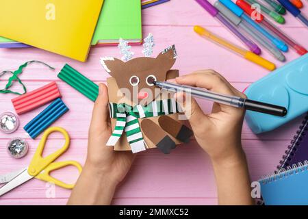 Frau, die Spielzeughirsche aus Toilettenpapier am pinkfarbenen Holztisch macht, Draufsicht Stockfoto
