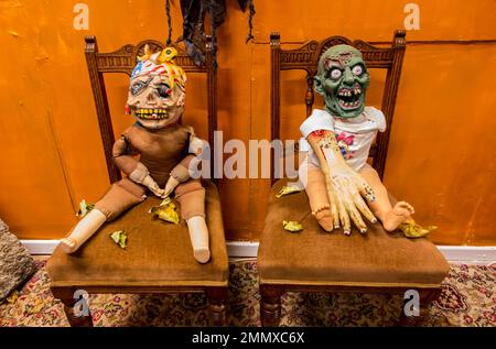 Halloween-Ausstellung von zwei unheimlichen Zombie-ähnlichen Kreationen, die auf alten Stühlen sitzen. Stockfoto