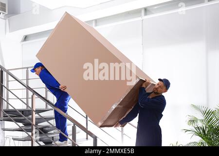 Professionelle Arbeiter, die Kühlschränke auf Treppen in Gebäuden tragen Stockfoto