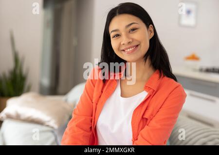 Porträt einer glücklichen, birassischen Frau, die zu Hause im Wohnzimmer lächelt, mit Kopierraum. Das Konzept der Freizeit, des Glücks und des häuslichen Lebens. Stockfoto