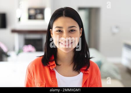 Porträt einer glücklichen, birassischen Frau, die zu Hause im Wohnzimmer lächelt, mit Kopierraum. Das Konzept der Freizeit, des Glücks und des häuslichen Lebens. Stockfoto