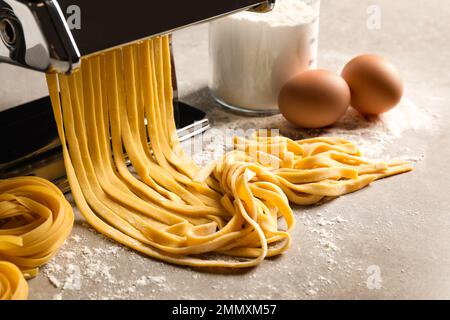 Pasta-Maschine mit Teig und Produkten auf grauem Tisch Stockfoto