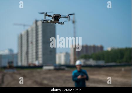 Ein Mann in Helm und Overall steuert eine Drohne auf einer Baustelle. Der Bauherr führt die technische Überwachung durch. Stockfoto