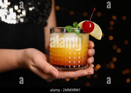 Frau mit einem Glas Tequila Sunrise auf verschwommenem Hintergrund, Nahaufnahme. Köstlicher alkoholischer Cocktail Stockfoto