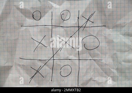 Das Spiel Tic-tac-toe wird mit einem Stift auf einem zerknitterten Notizbuch in einem Käfig gezeichnet, spielen und ruhen, Kinderspiel Tic-tac-toe Stockfoto