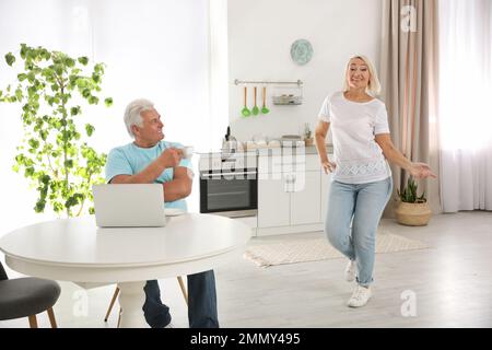 Eine Frau mittleren Alters, die neben ihrem Mann in der Küche tanzt. Glückliches reifes Paar Stockfoto