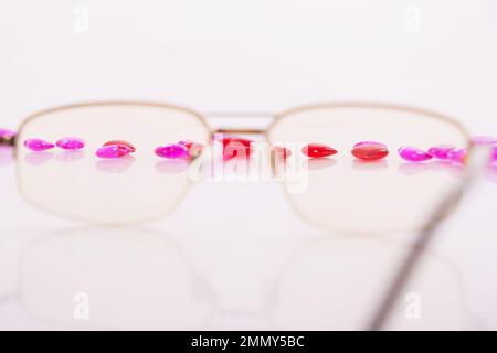 Tabletten, Kapseln zum Sehen. Vitamine in Form von Herzen mit Brille auf weißem Hintergrund. Dioptrien, Myopie, Weitsicht. Augenarzt, Optiker, Augengesundheit. Hochwertiges Foto Stockfoto