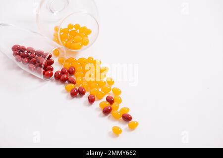 Tabletten, Kapseln zum Sehen. Rote und gelbe Vitamine werden aus dem Glas auf den Tisch gegossen. Dioptrien, Myopie, Weitsicht. Gesunder Körper, Herz und Knochen. Hochwertiges Foto Stockfoto