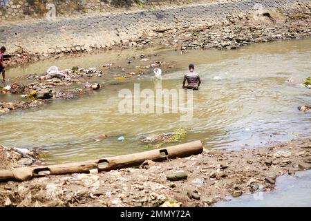 Ein Mann gräbt durch den Müll, der auf dem Fluss schwimmt, auf der Suche nach etwas von Wert. Bali, Indonesien - 03.01.2018 Stockfoto