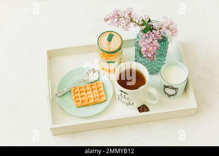 Frühstück mit Tee, Waffeln und Fliederblumen auf dem Tablett Stockfoto