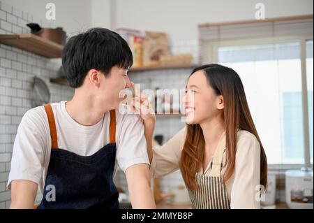 Ein junges asiatisches Paar, das beim Kochen von Speisen in der Küche spielt, romantische Momente in der Küche verbringt, genießt das Wochenende zu Hause. Stockfoto