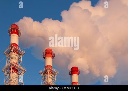 Drei industrielle Schornsteine, die weißen Rauch gegen einen blauen Himmel ausstrahlen. Stockfoto