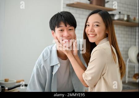 Glückliches, junges asiatisches Paar, das zu Hause eine glückliche Zeit hat, ein sorgenfreies Wochenende miteinander verbringt, sich Liebe zeigt, romantische Momente in der Ki genießt Stockfoto