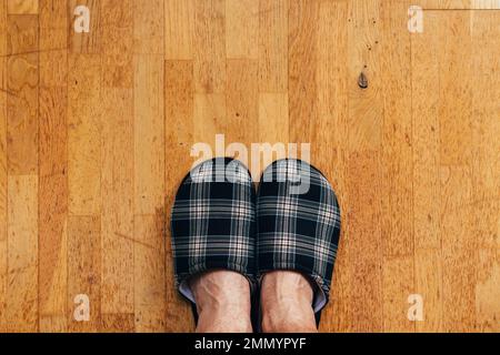 Draufsicht auf männliche Füße, die Heimschuhe tragen und auf dem Hartholzboden im Wohnzimmer stehen, Kopierbereich inbegriffen Stockfoto