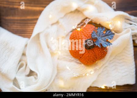 Orangefarbener Kürbis, eingewickelt in einem warmweißen Karo mit Lichtern von Girlanden, auf einem Holztisch mit Kopierraum. Herbststimmung, halloween, Ernte, Thanksgiving, Stockfoto