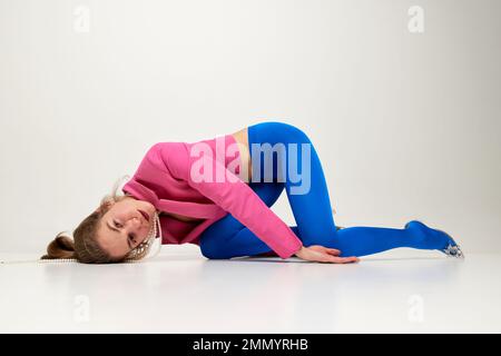 Emotionales junges, stilvolles Mädchen in blauen Strumpfhosen und rosa Croptop posieren, auf dem Boden isoliert auf grauem Hintergrund seltsame Posen machen. Das Konzept von "seltsam" Stockfoto