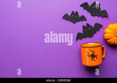 Orangefarbene Tasse auf lila Hintergrund mit schrecklichen Halloween-Dekorationen. Das Konzept der Halloween-Feiertage. Trinken, Spaß, Party. Raum kopieren, Modell erstellen, f Stockfoto