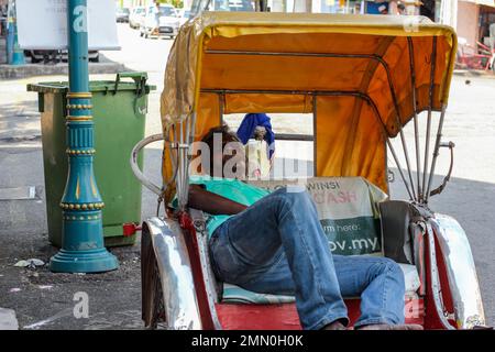 Georgetown, Penang, Malaysia - November 2012: Ein Rikscha-Fahrer macht ein Nickerchen in seinem Fahrzeug, das auf einer Straße geparkt ist. Stockfoto