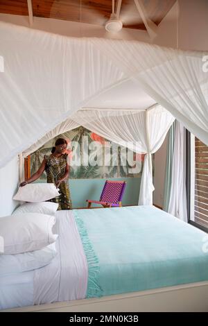 Senegal, Saloum Delta, UNESCO-Weltkulturerbe, Palmarin, Patricks Lodge, Haushälterin in einem Wachskleid, die in einer Suite mit tropischem Dekor ein Kissen auf ein Himmelbett legt Stockfoto