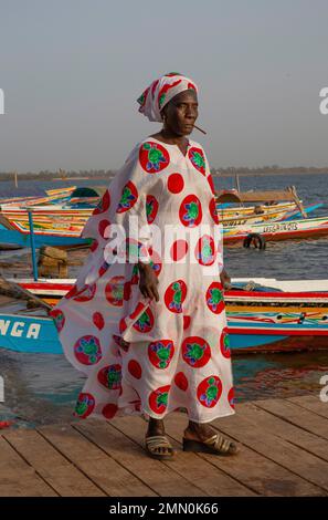 Senegal, Saloum Delta, UNESCO-Weltkulturerbe, Frau in farbenfrohem Boubou inmitten von Kanus auf dem Ponton des Ndangane Pier Stockfoto