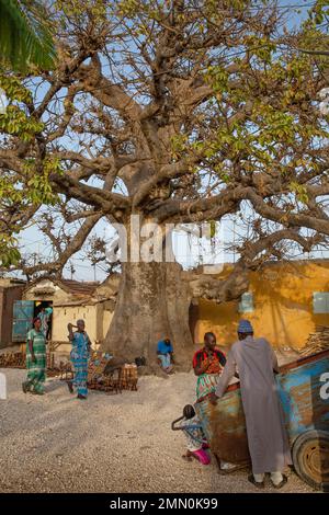 Senegal, Saloum Delta, das von der UNESCO zum Weltkulturerbe erklärt wurde, Fadiouth oder die Muschelinsel, imposanter Baobab-Wanderhändler und Frauen in Boubou auf einem Dorfplatz Stockfoto