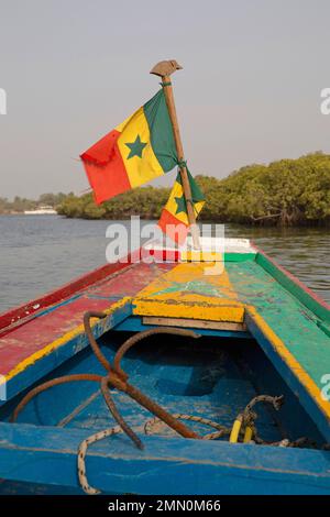 Senegal, Saloum-Delta, UNESCO-Weltkulturerbe, senegalesische Flagge, die an der Vorderseite eines mehrfarbigen Kanus hängt, das in der Mitte der Mangroven segelt Stockfoto