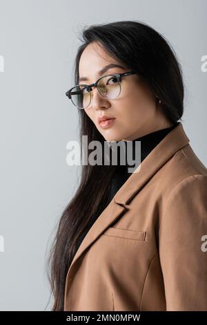 Junge asiatische Geschäftsfrau in Brille und Blazer, die isoliert auf Grau auf die Kamera schaut Stockfoto
