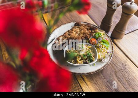 Paniertes gebratenes Schweinefleisch Schabowy serviert mit gekochten Kartoffeln und Salat auf weißem Teller. Polnische Küche. Horizontale Indoor-Aufnahme. Hochwertiges Foto Stockfoto