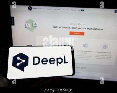Person, die ein Mobiltelefon mit dem Logo des neuronalen maschinellen Übersetzers DeepL auf dem Bildschirm vor der Webseite hält. Konzentrieren Sie sich auf das Display des Telefons. Stockfoto